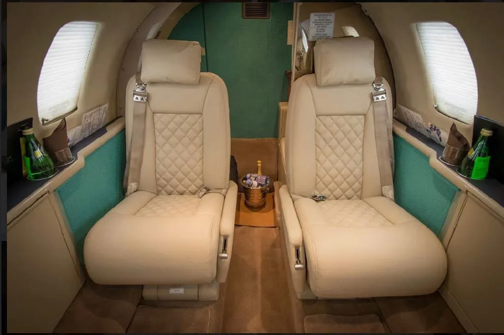Two quilted beige leather seats in the private jet cabin, with small bottles of water on side tables.