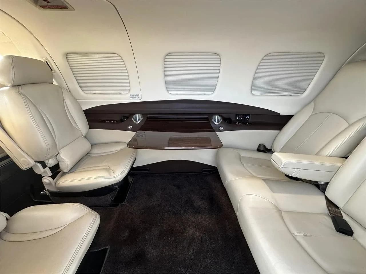 The cabin interior of the Piper M350 aircraft, with light-colored leather seats and a fold-out table on the side panel.