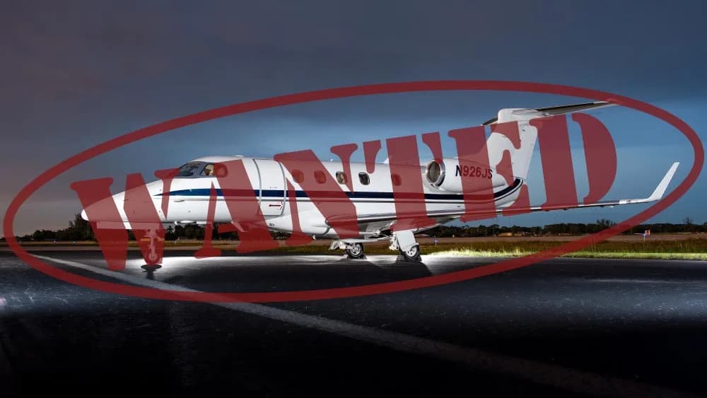 A white business jet with blue stripes, registration N926JS, is parked on a tarmac at night with ground lighting.