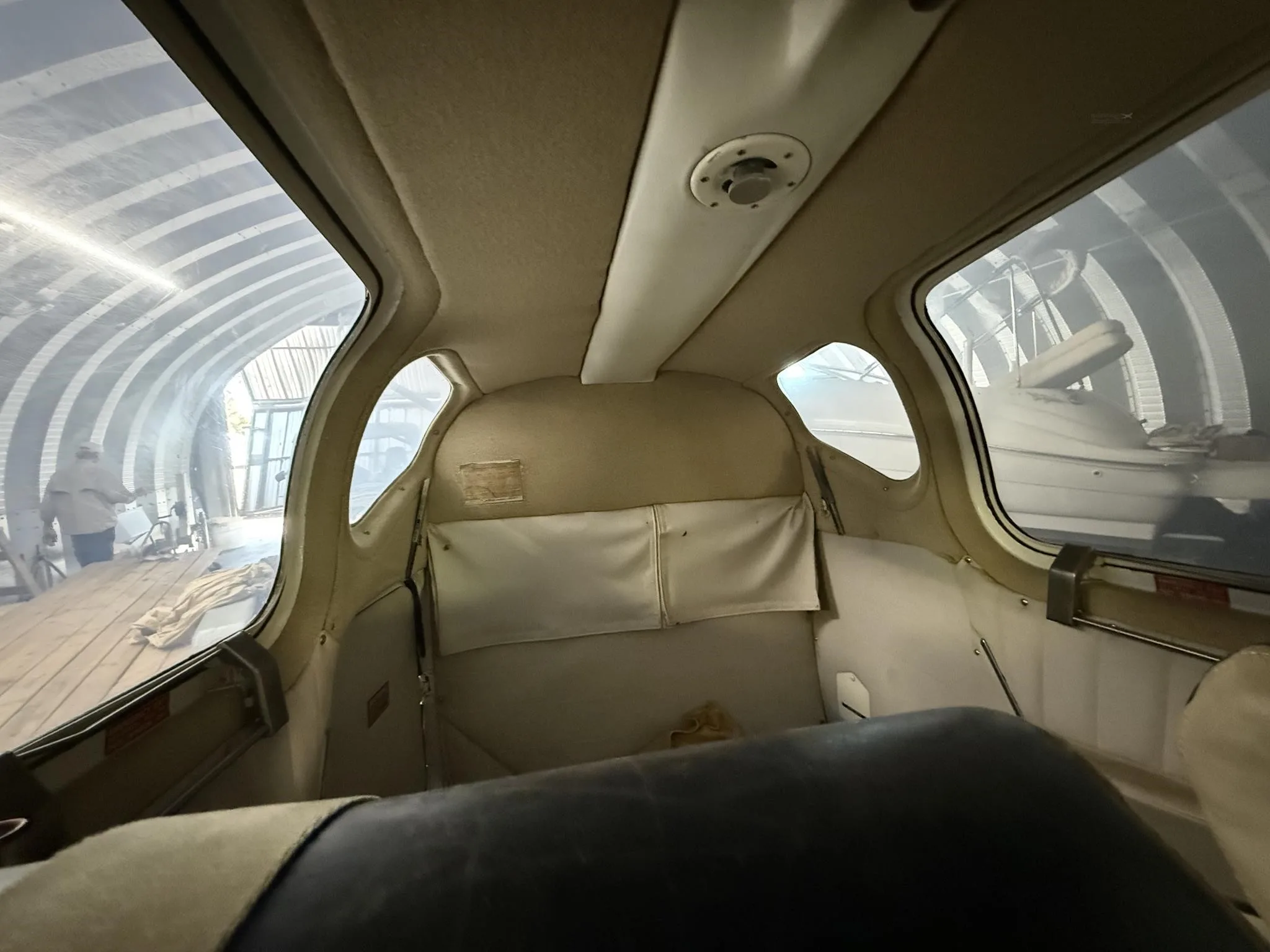 The aircraft's rear cabin interior with tan upholstery and storage pockets, looking towards the front.