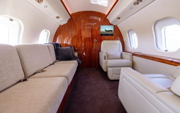 Aircraft cabin interior with cream-colored leather seats and a table.