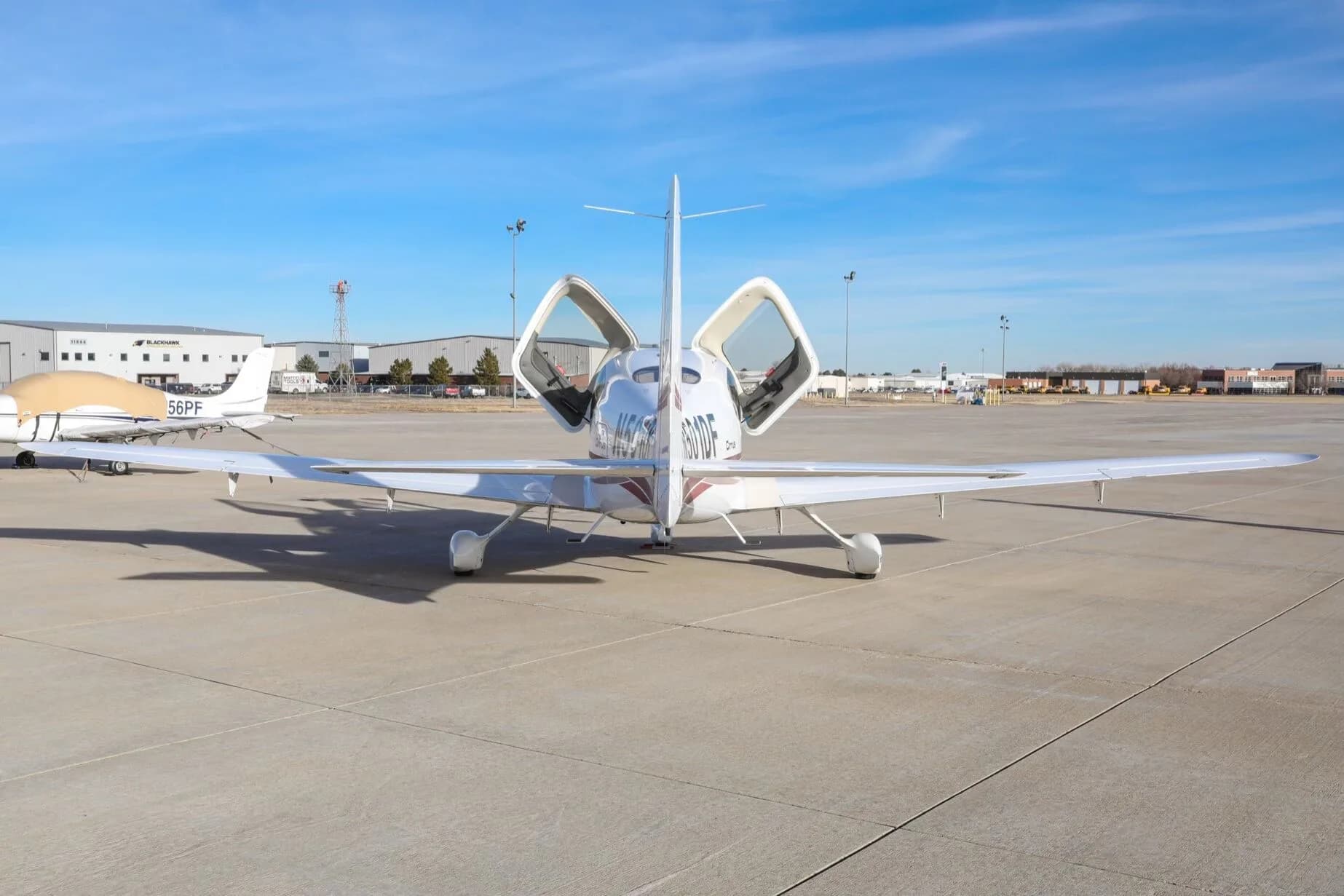Rear view of a white Cirrus SR20 aircraft with its gull-wing doors open, parked on an airfield.