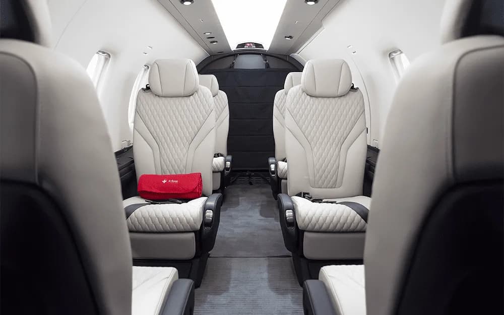 The luxurious white and black quilted leather interior cabin of the Pilatus PC-12 NGX, with a red bag on a seat.