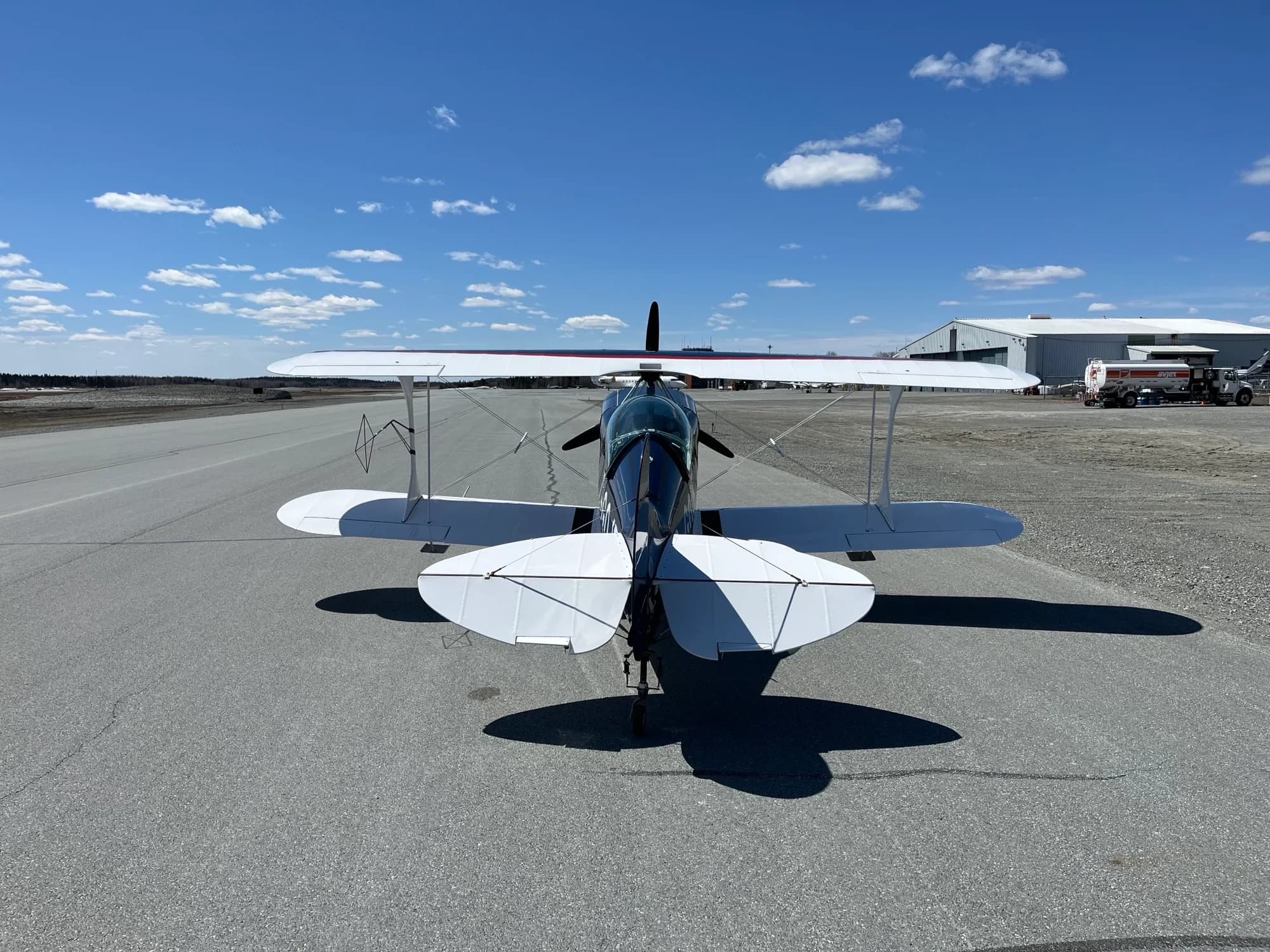 A rear view of the dark blue and white Pitts biplane C-GOJF parked on an asphalt runway.