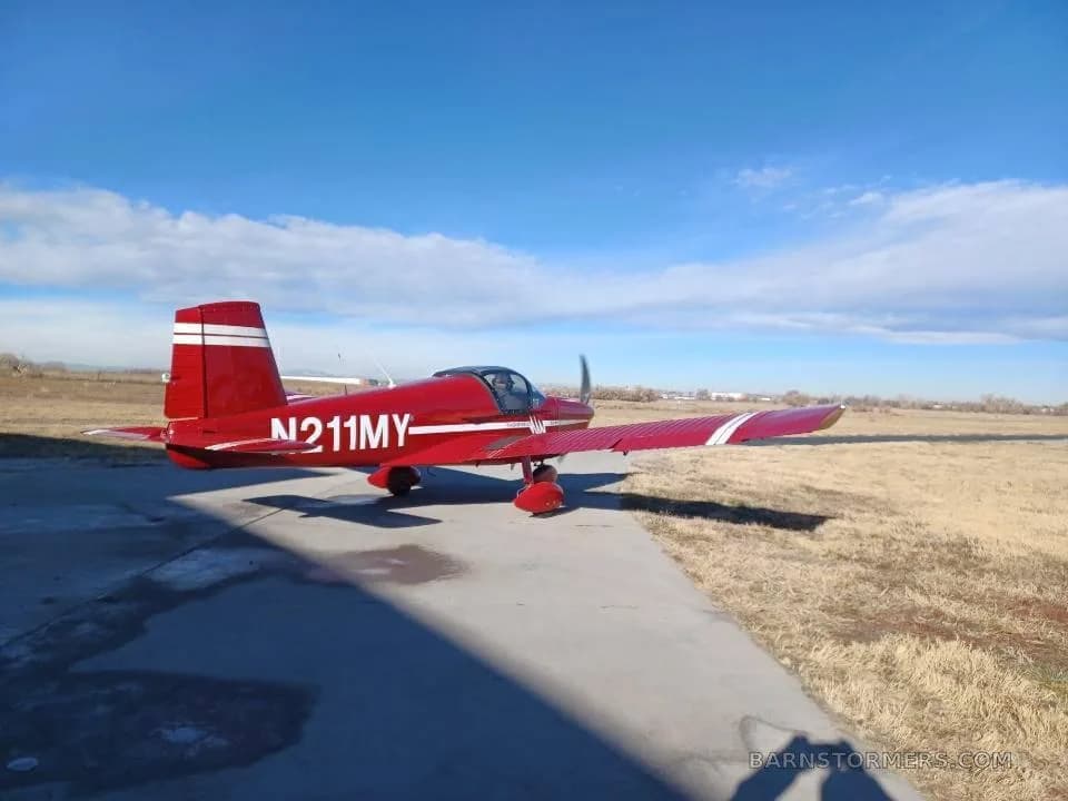 A red Thorp T211 Torpedo aircraft with white stripes and registration N211MY, parked on a concrete pad at an airfield under a blue sky.