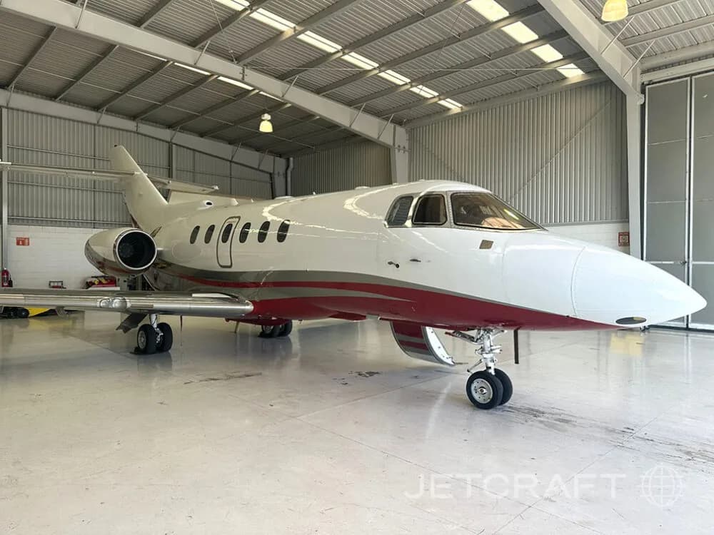 A white and red business jet with its nose facing right, parked inside a hangar.