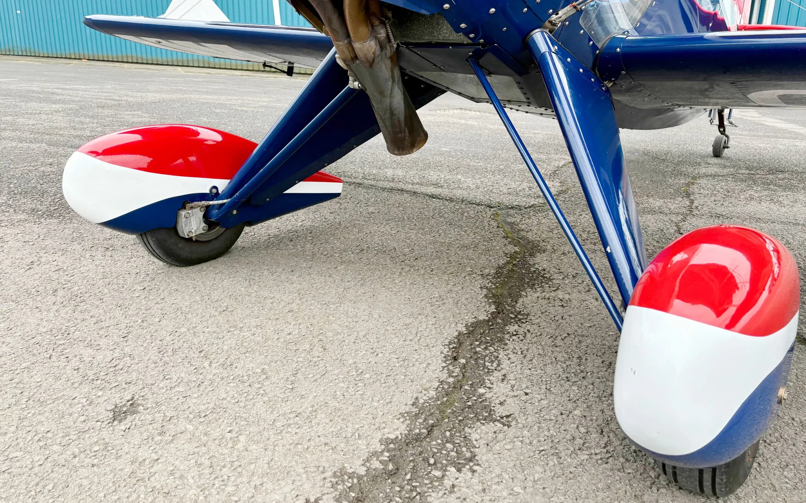 A close-up view of the red, white, and blue main landing gear and wheel fairings of the Pitts S1T biplane.