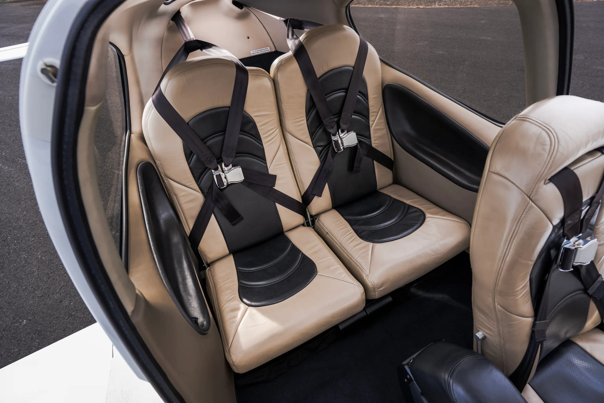 An overhead view of the rear cabin seats, upholstered in tan and black leather with seatbelts.