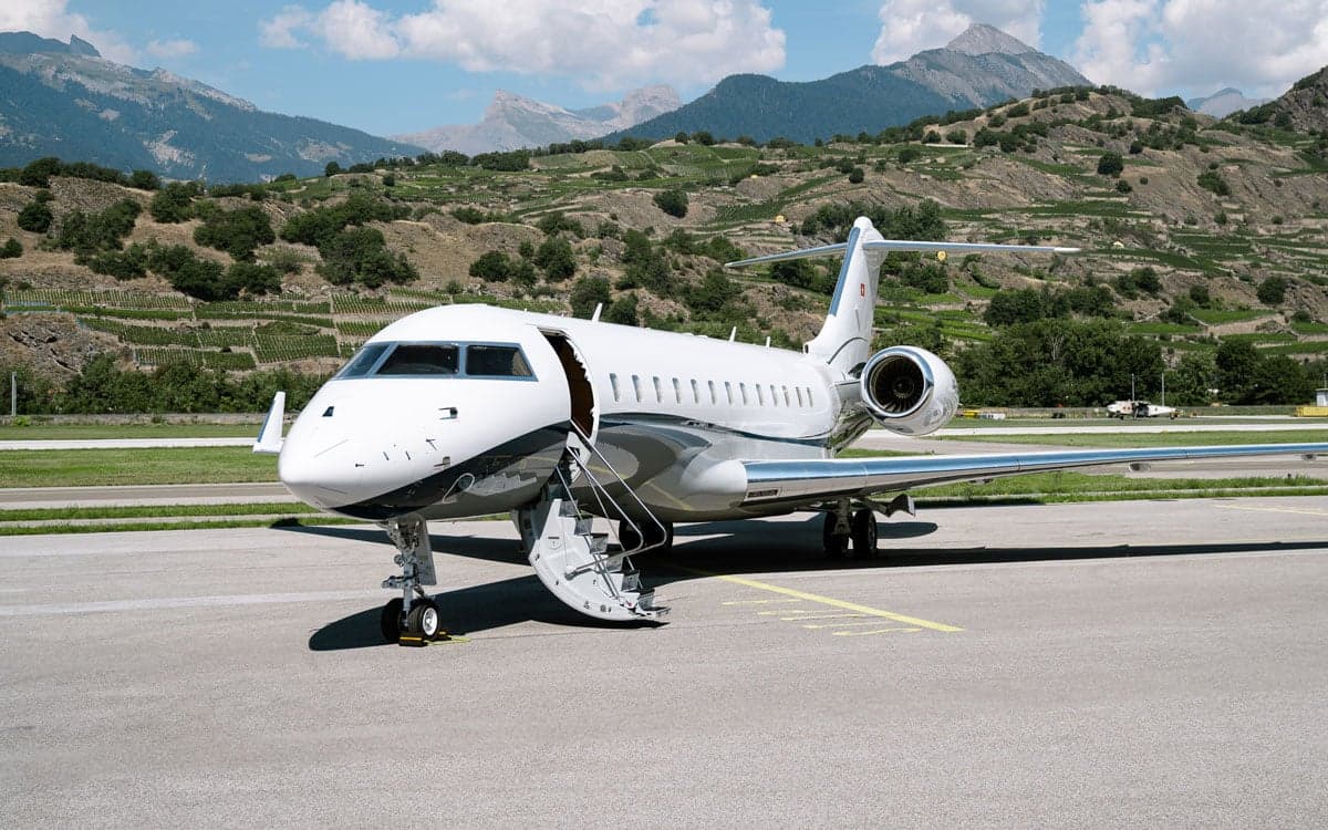 A Bombardier Global XRS aircraft parked on the tarmac with mountains in the background.