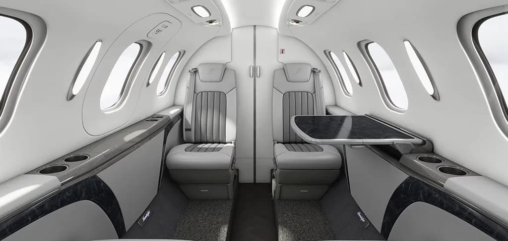 The luxurious interior cabin of a HondaJet, featuring light gray leather seats, a dark table, and large windows.