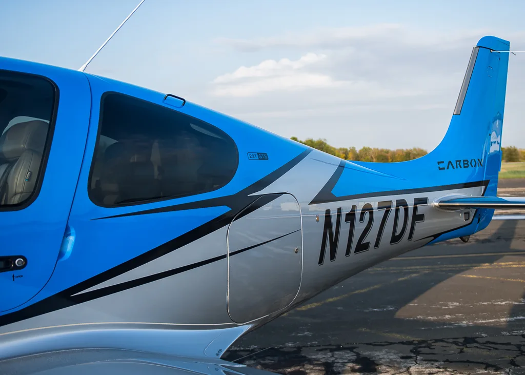 A close-up view of the blue and silver fuselage and tail of the Cirrus SR22T GTS Carbon aircraft (N127DF), showing the "CARBON" branding.