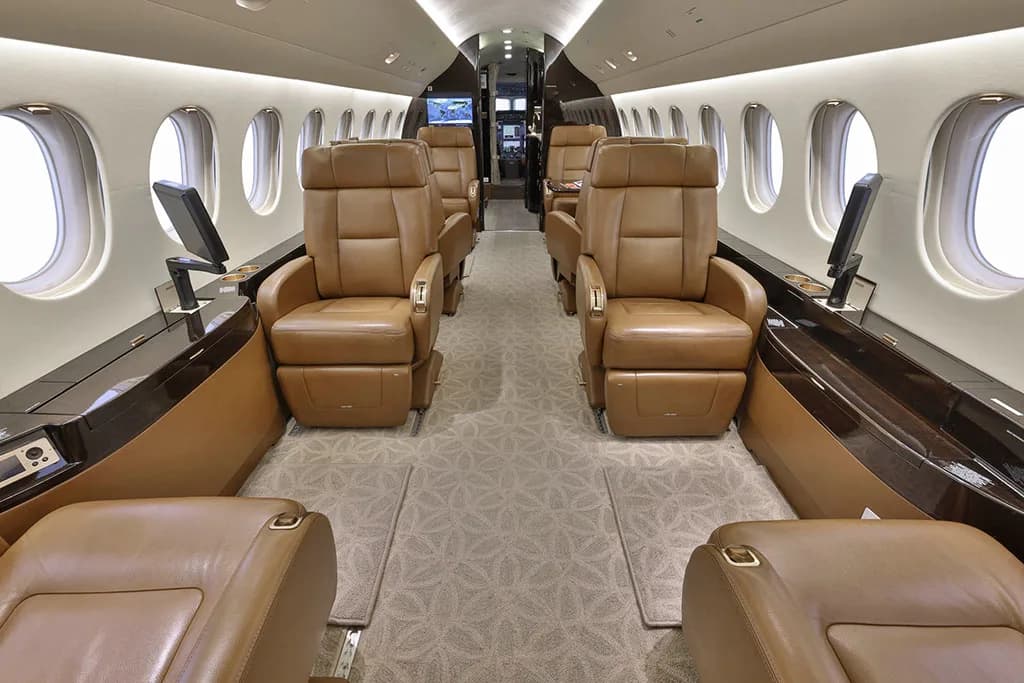The luxurious interior cabin of a business jet features rows of tan leather seats and large oval windows.
