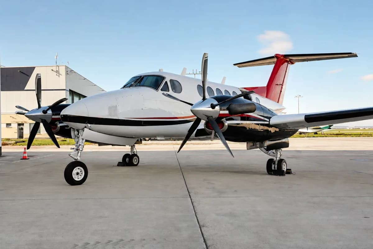 A white and red twin-engine turboprop aircraft with registration OK-MAG parked on the tarmac next to a building.