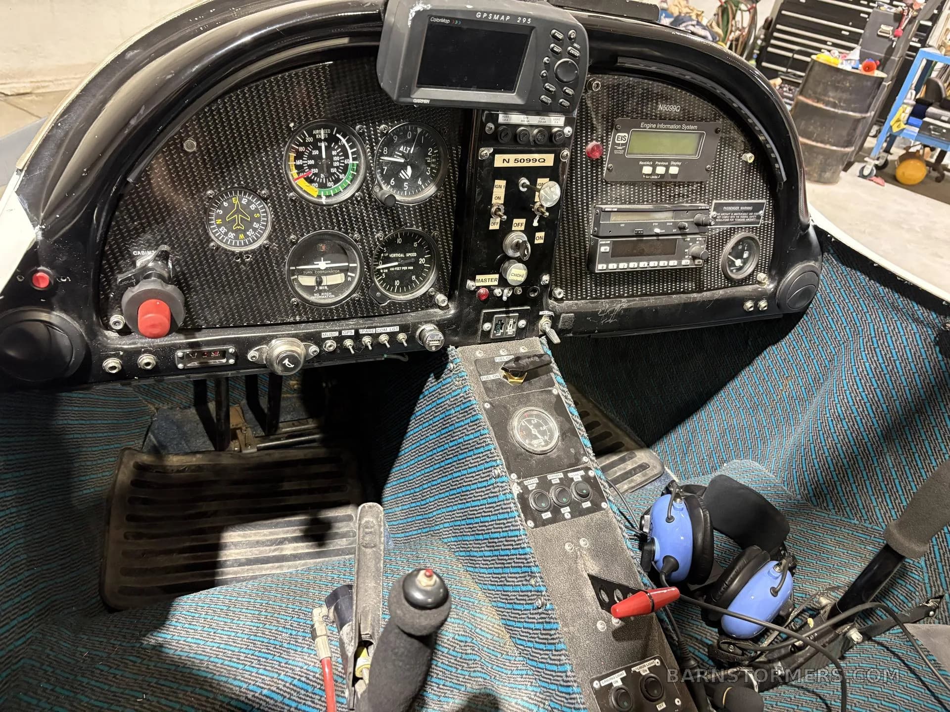 The cockpit of an experimental aircraft, featuring a carbon fiber instrument panel with various gauges, a GPS unit, and blue patterned upholstery.