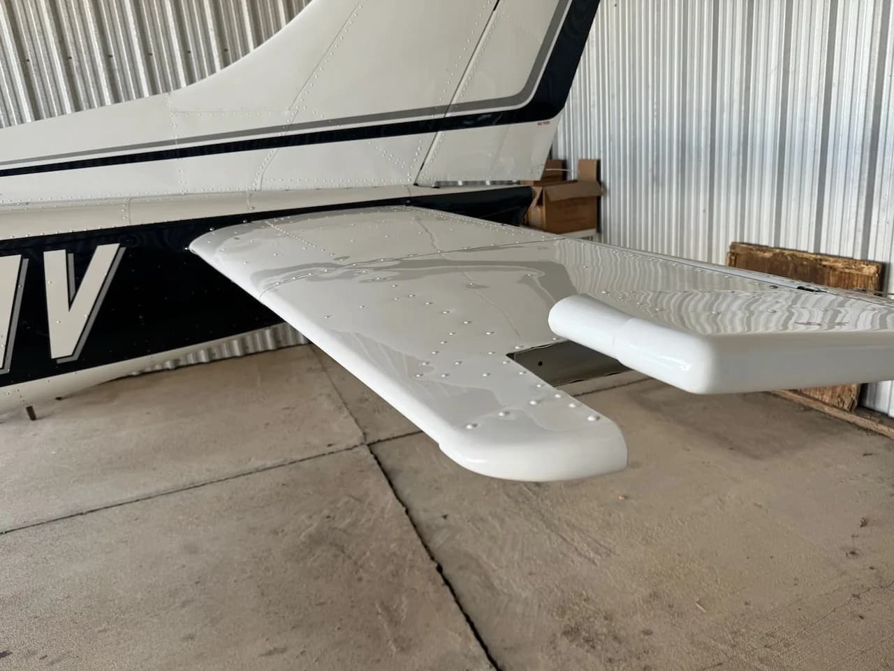 A close-up view of the white horizontal stabilizer and elevator of an aircraft, inside a hangar.