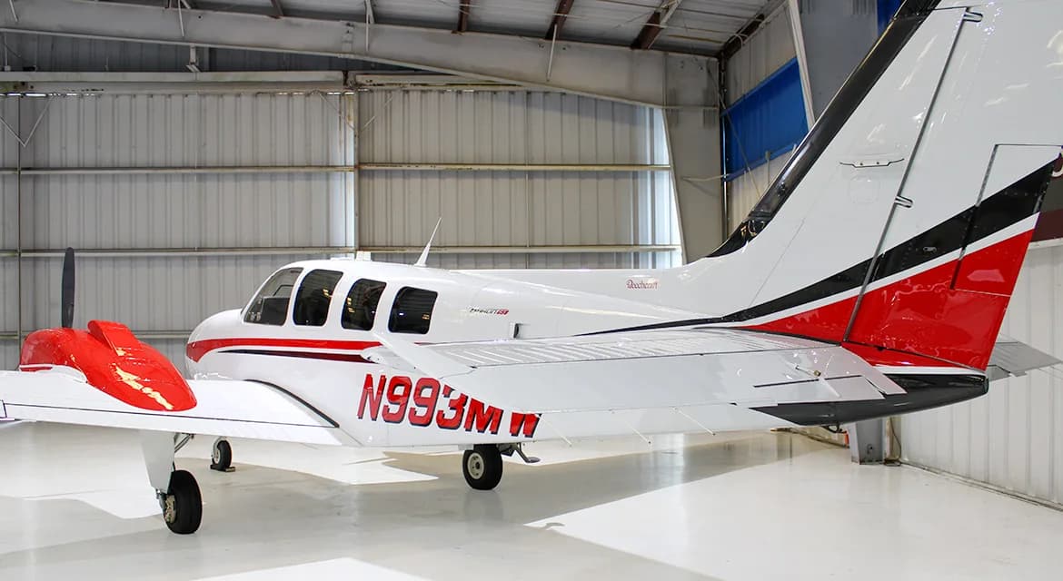 A rear-quarter view of a white and red twin-engine propeller aircraft, a Beechcraft Baron, showing tail number N993MW.