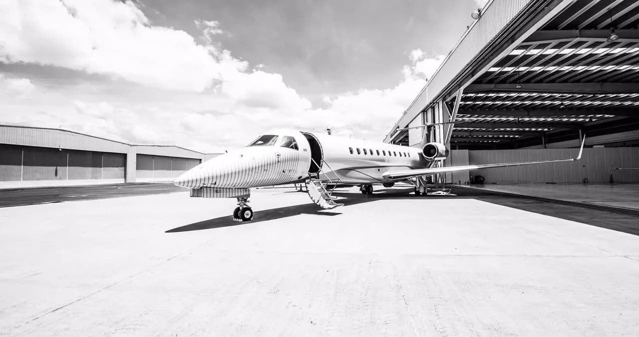 A black and white photo of a white Embraer Legacy 600 business jet parked outside a hangar with its main door open.