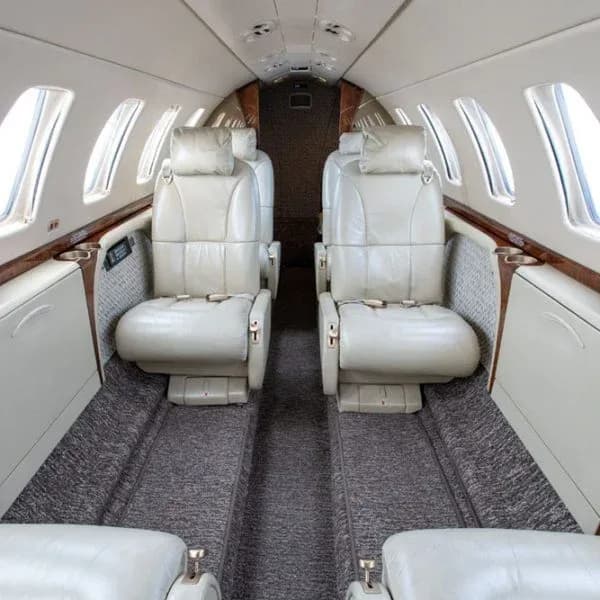 A slightly wider interior view of an aircraft cabin featuring light beige leather seats and patterned carpet.