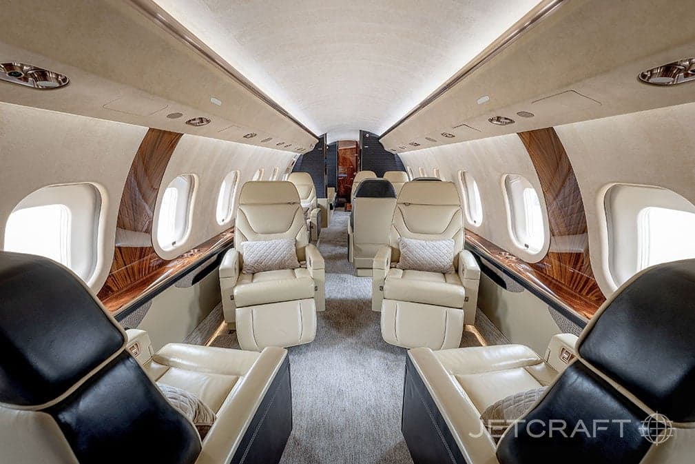 Forward view of the aircraft cabin with tan leather seats and wood trim.