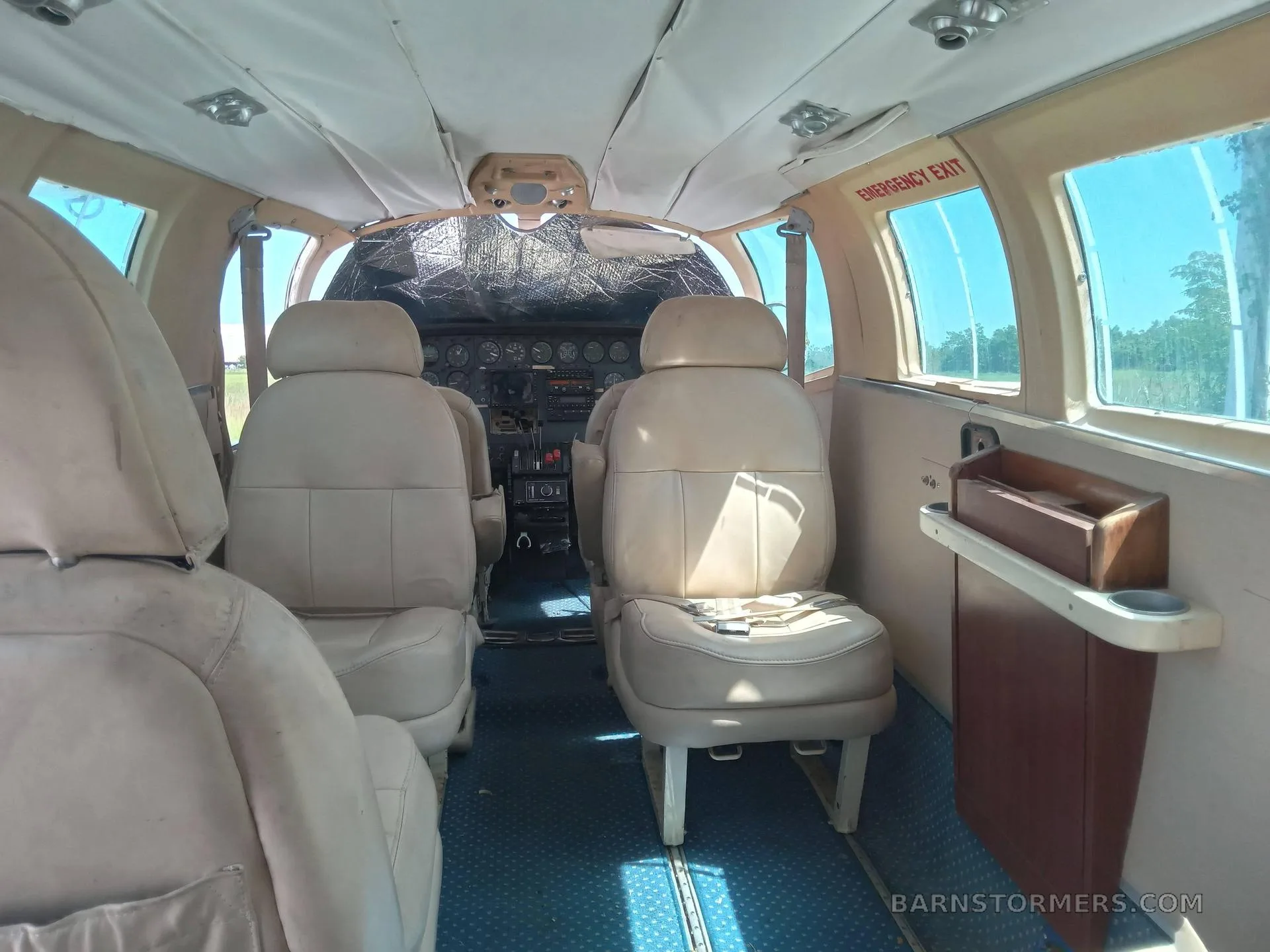 The interior cabin of a small aircraft, showing beige passenger seats and a blue patterned carpet, looking towards the cockpit which is covered by a sunshade.
