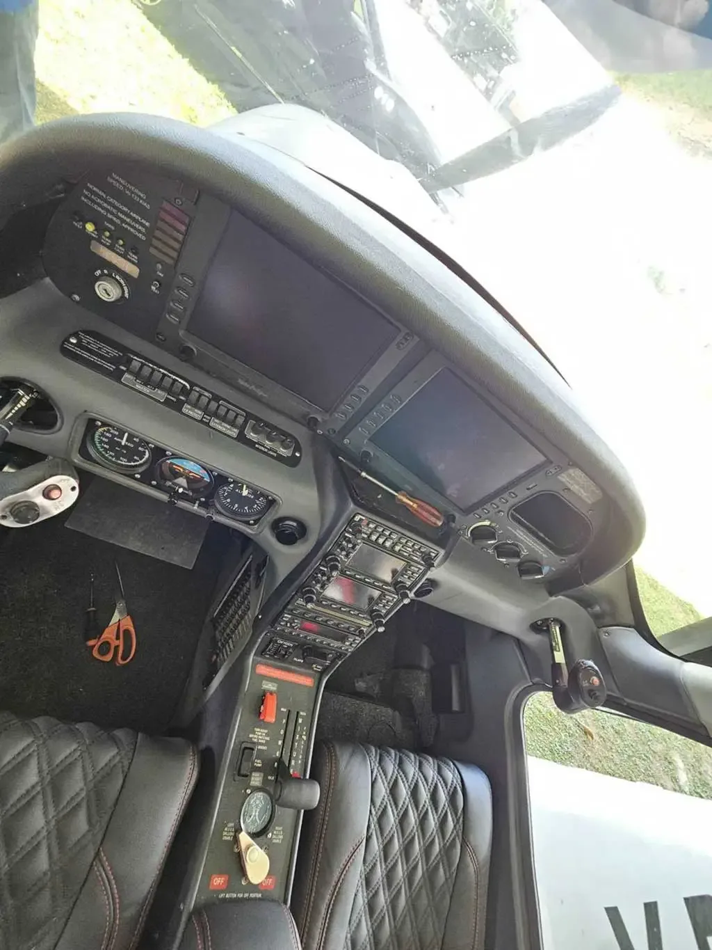 A wide-angle view of an aircraft's cockpit, showing the instrument panel with multiple screens, controls, and black leather seats.