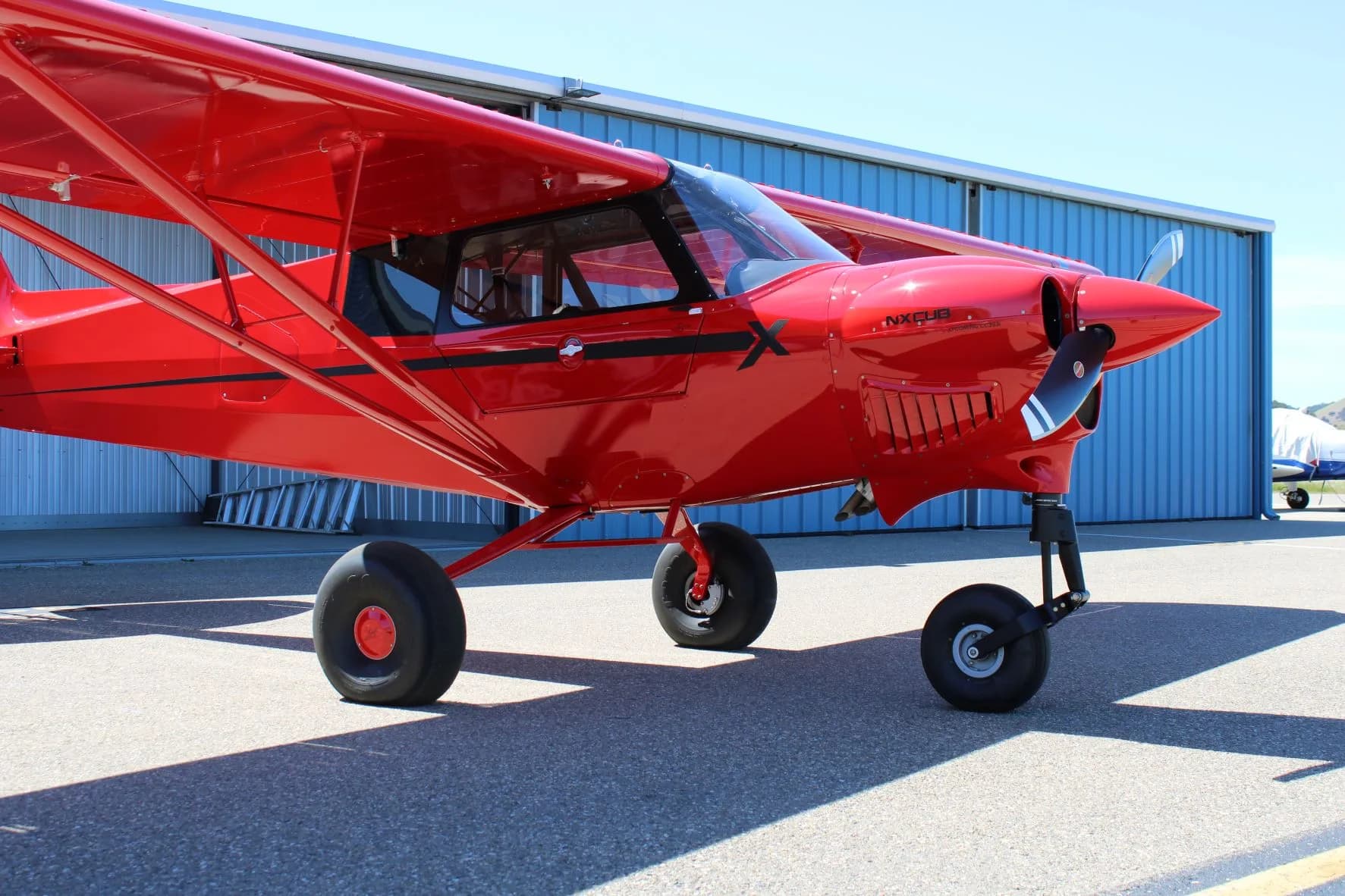 Side view of the red NX Cub aircraft parked on the tarmac in front of a hangar.