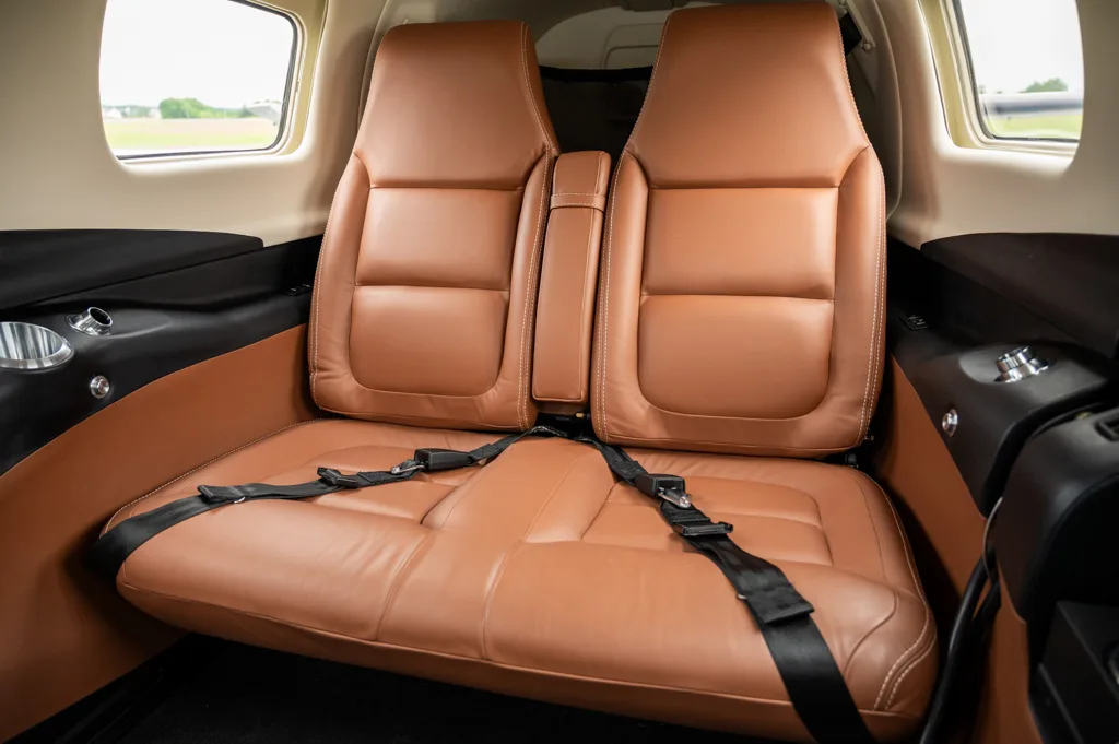 A close-up view of the tan leather rear seats with black seatbelts in an aircraft cabin.
