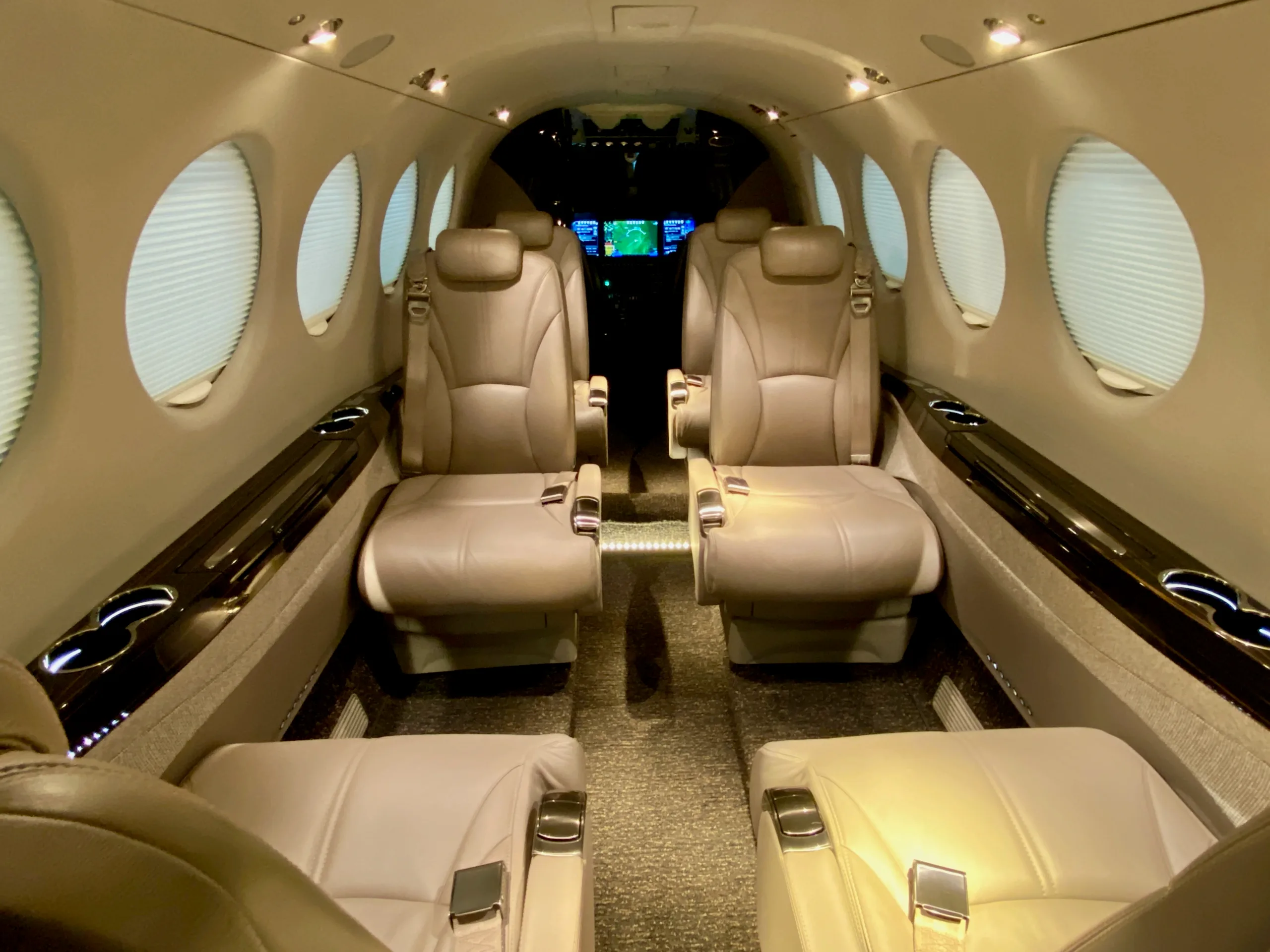 The interior cabin of an aircraft, featuring light-colored leather seats and oval windows with shades.