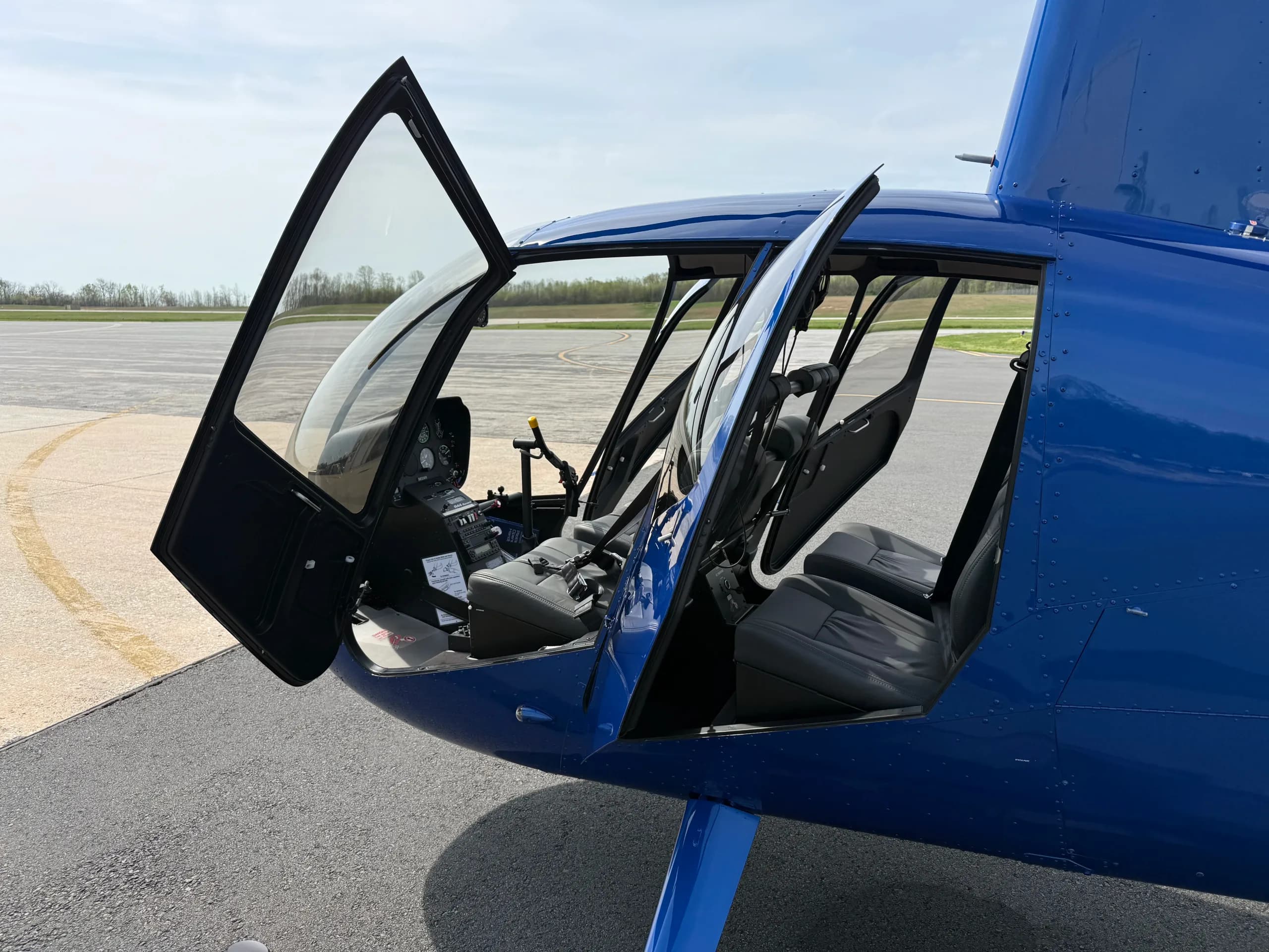 The open doors of a blue Robinson R44 helicopter revealing the gray interior seats and part of the cockpit.