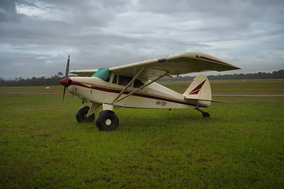 A cream and maroon single-engine taildragger aircraft with registration VH-TSY parked on a grassy airfield under a cloudy sky.
