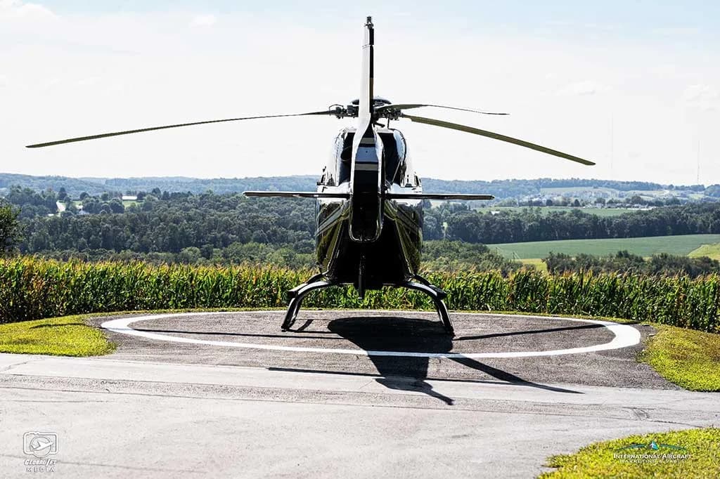 Rear view of a black Eurocopter AS350 helicopter (N123PE) on a helipad overlooking a rural landscape.