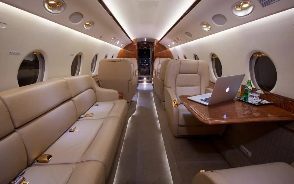 A luxurious aircraft cabin with tan leather seating, a sofa, and a table with a laptop.