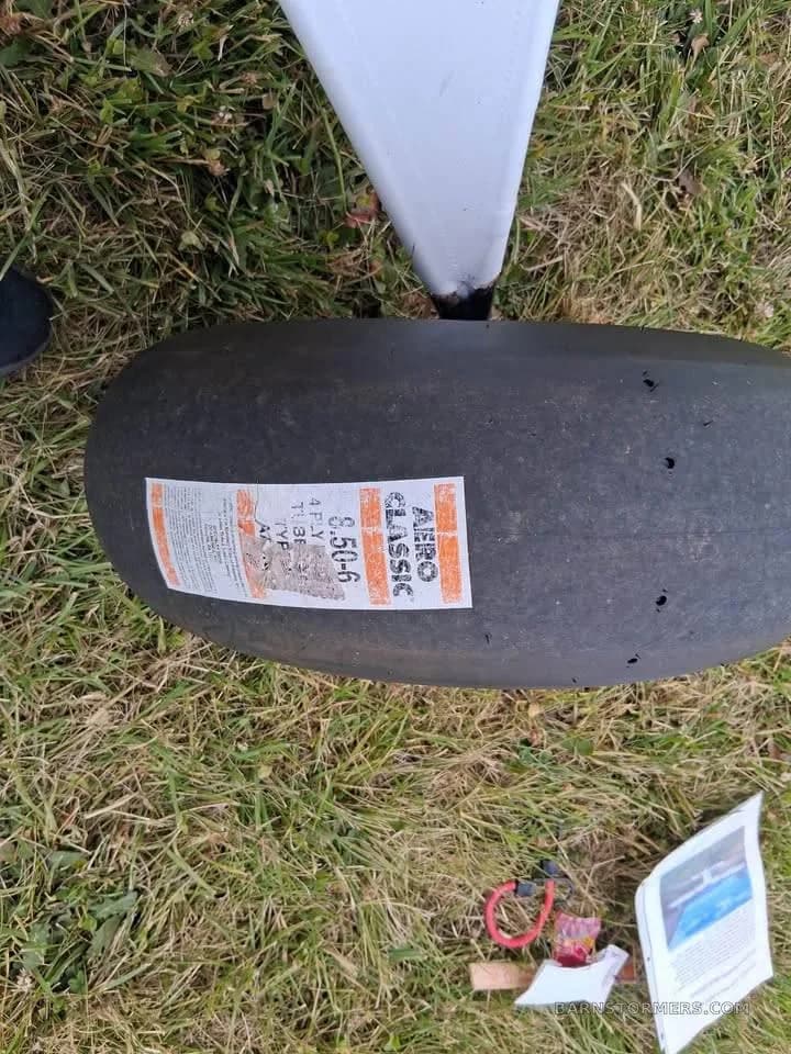 A close-up overhead view of a large "AERO CLASSIC" aircraft tire with a label on a grassy surface.