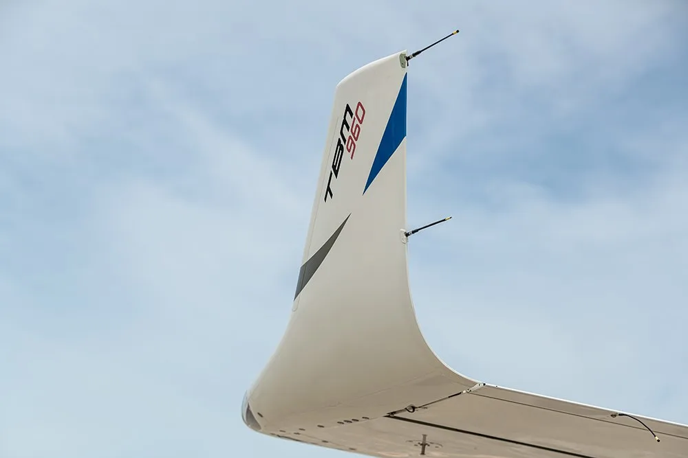 A close-up of the TBM 960 aircraft's wingtip with a blue and black accent against a cloudy sky.
