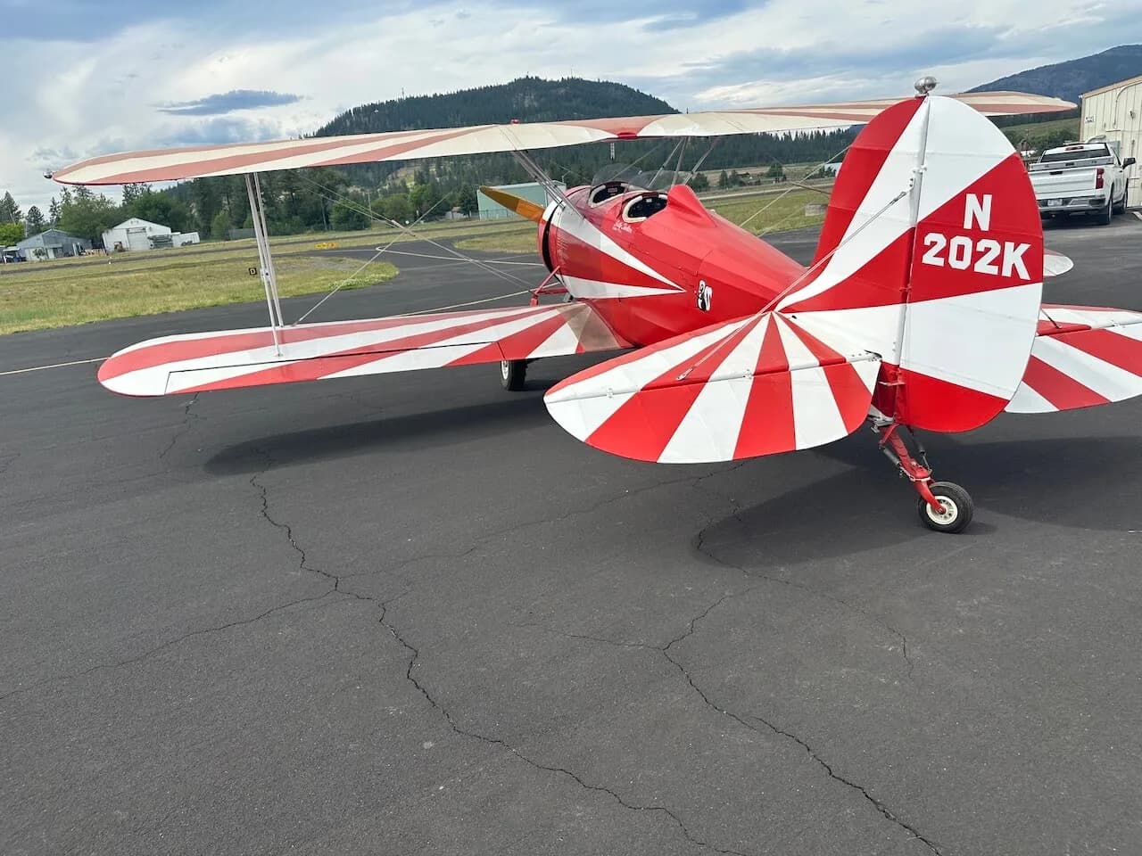 A red and white biplane with N202K on the tail, parked on an asphalt apron with a mountain in the background.