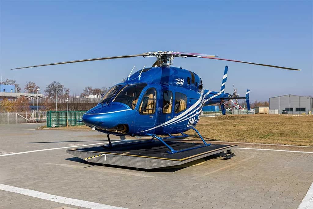 A blue helicopter with white stripes, registration OM-TIP, on a helipad under a clear sky.