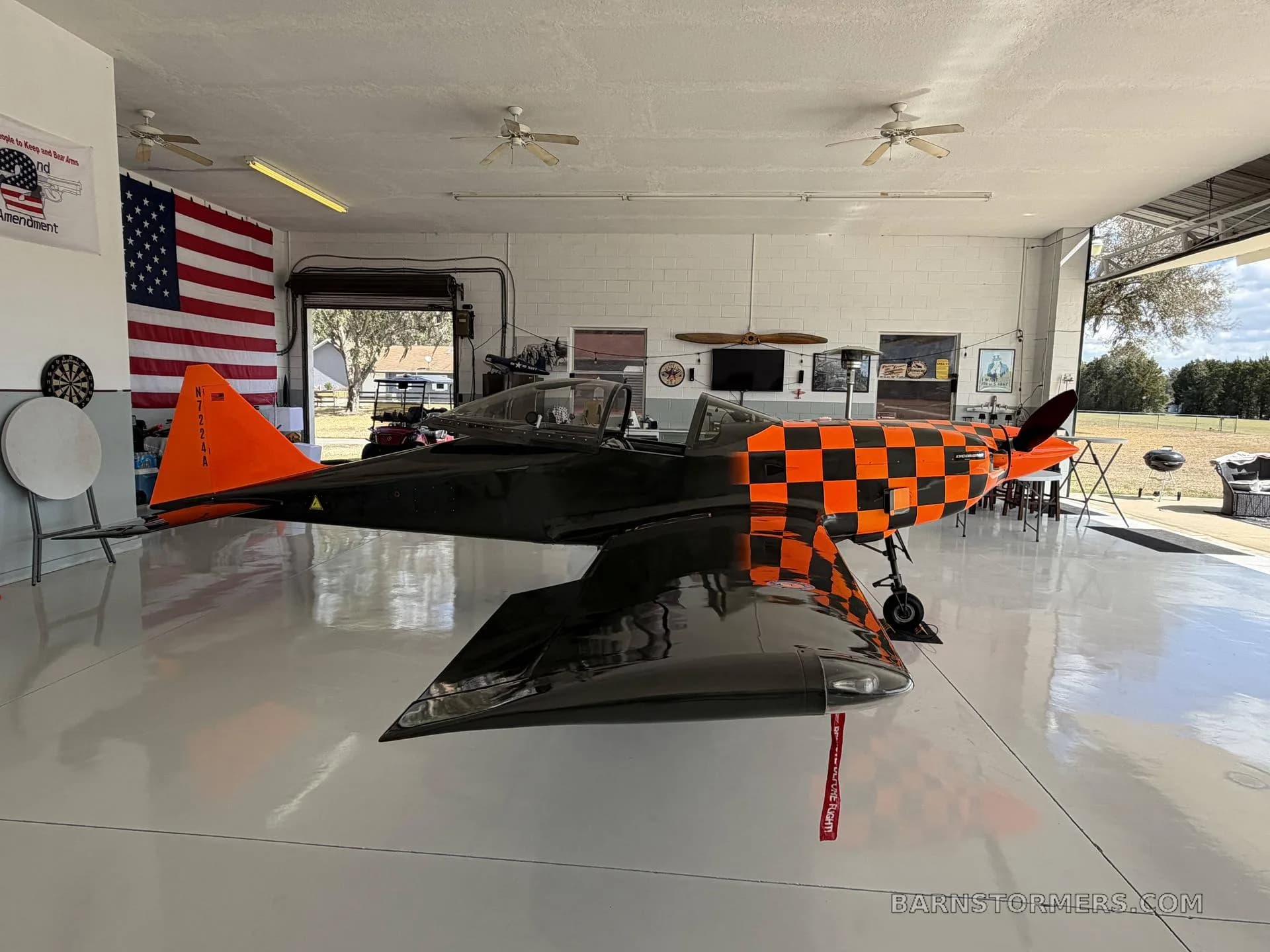 A black and orange checkered single-engine aircraft with tail number N7224A is parked inside a hangar.