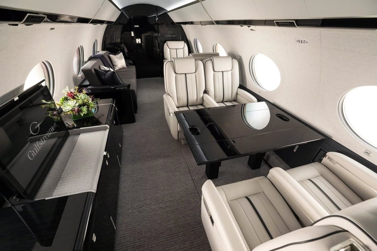 The interior of a Gulfstream jet, featuring white leather seats and a black table.