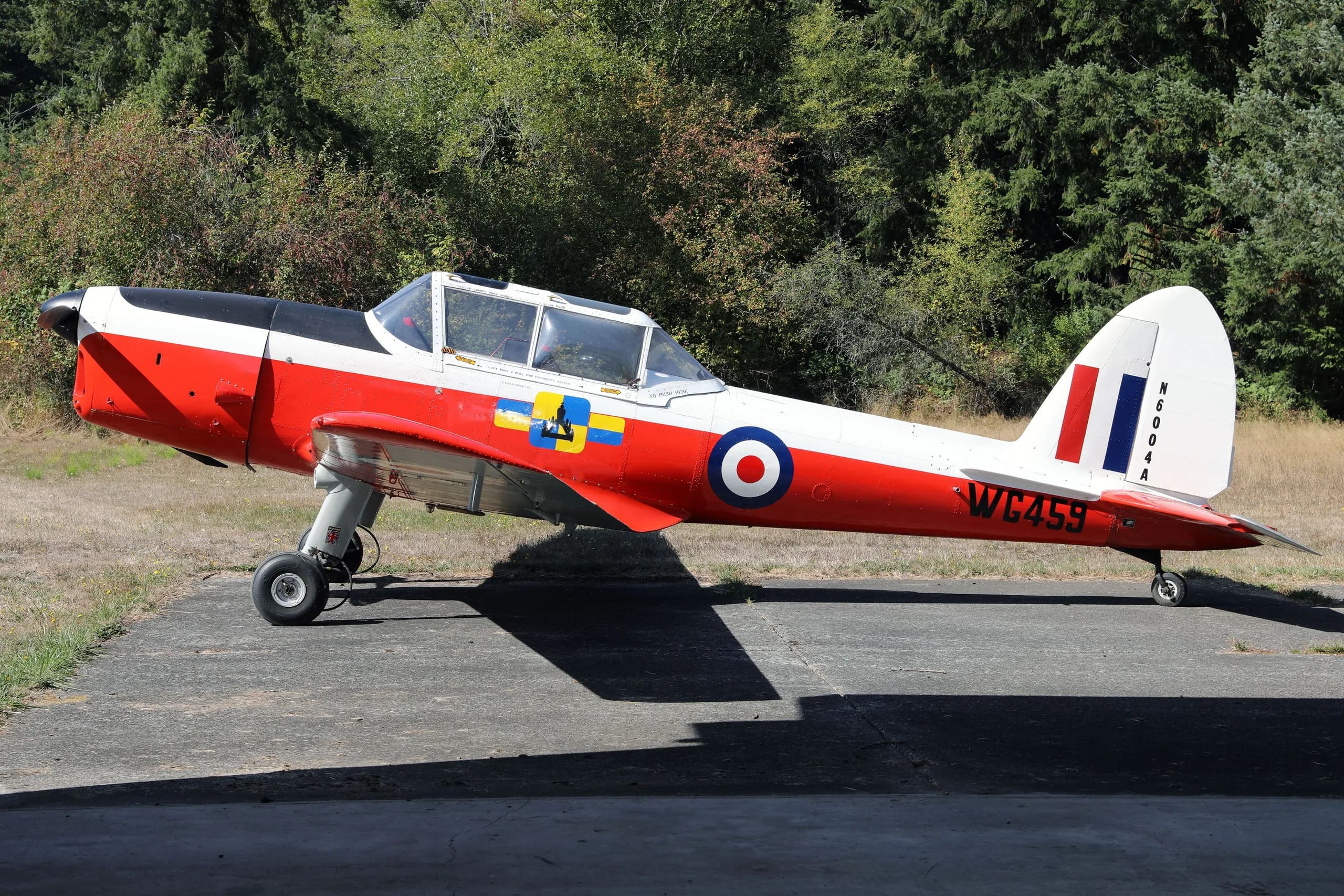 A red, white, and black de Havilland Canada DHC-1 Chipmunk aircraft with British roundels and "WC459" markings, parked on an airfield.