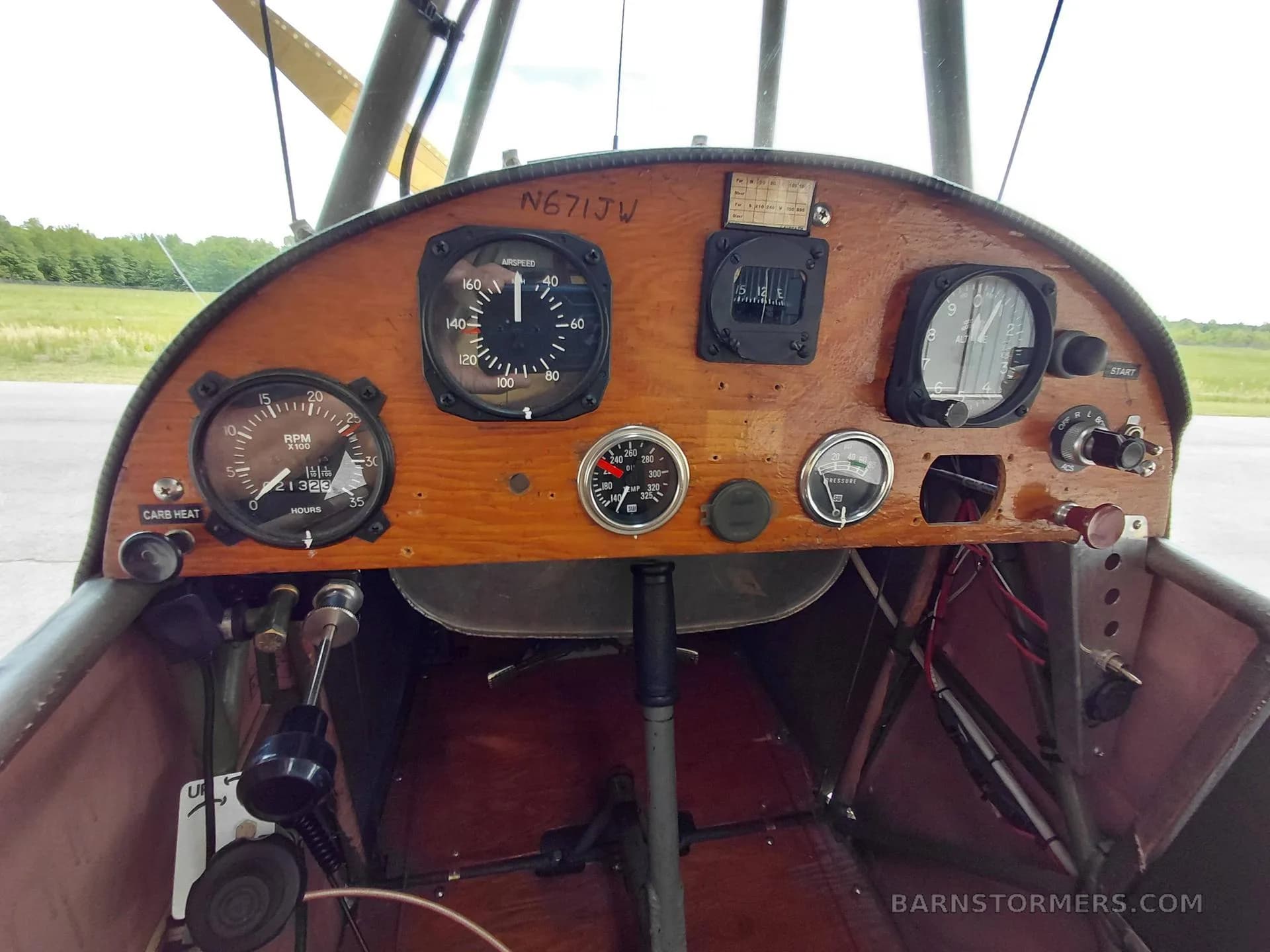 The wooden instrument panel of a vintage aircraft, showing a speedometer, RPM gauge, altimeter, and other controls.