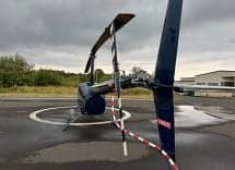 A blue Robinson R44 helicopter on a helipad, viewed from the rear.