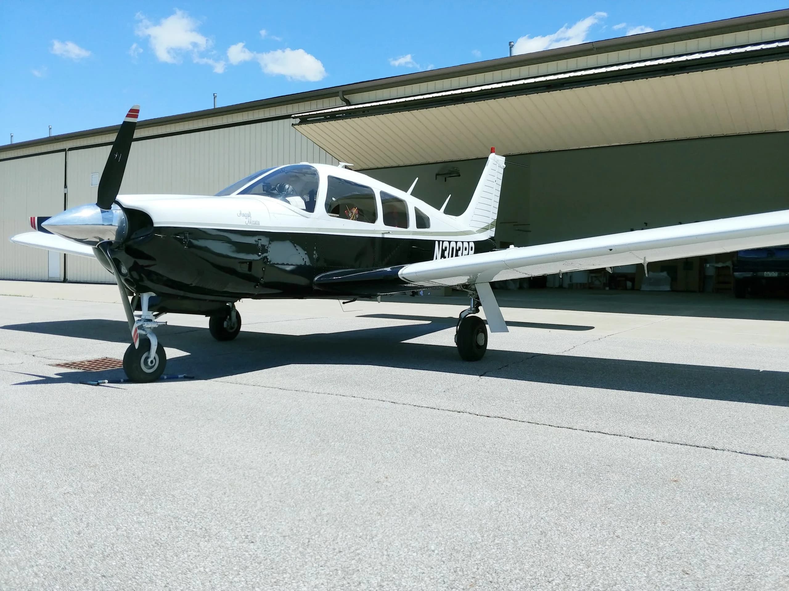 A black and white Beechcraft Bonanza sits on the tarmac in front of an open hangar.