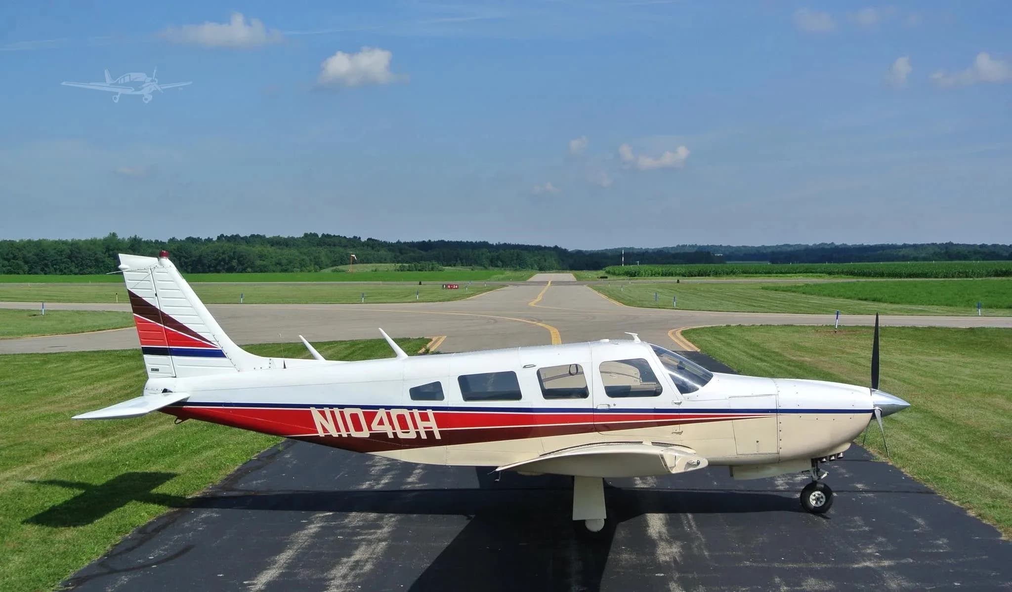 A side profile view of a white and beige single-engine aircraft with red and blue stripes on an asphalt runway under a clear blue sky.