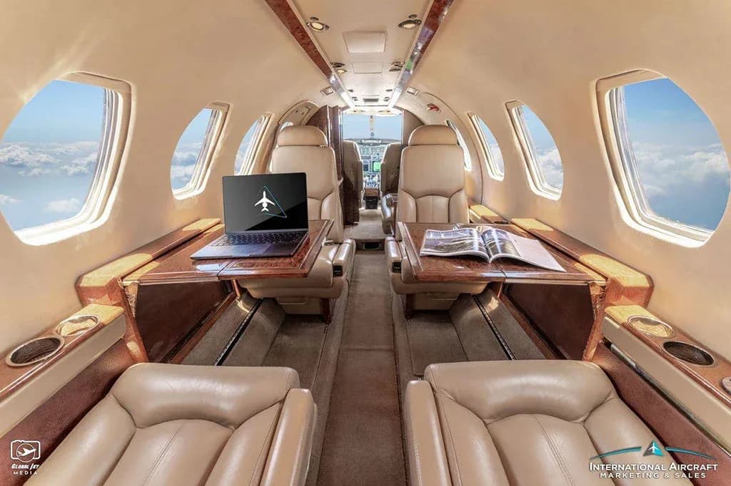 The tan leather interior of the Cessna Citation V cabin with a laptop and magazine on fold-out tables.