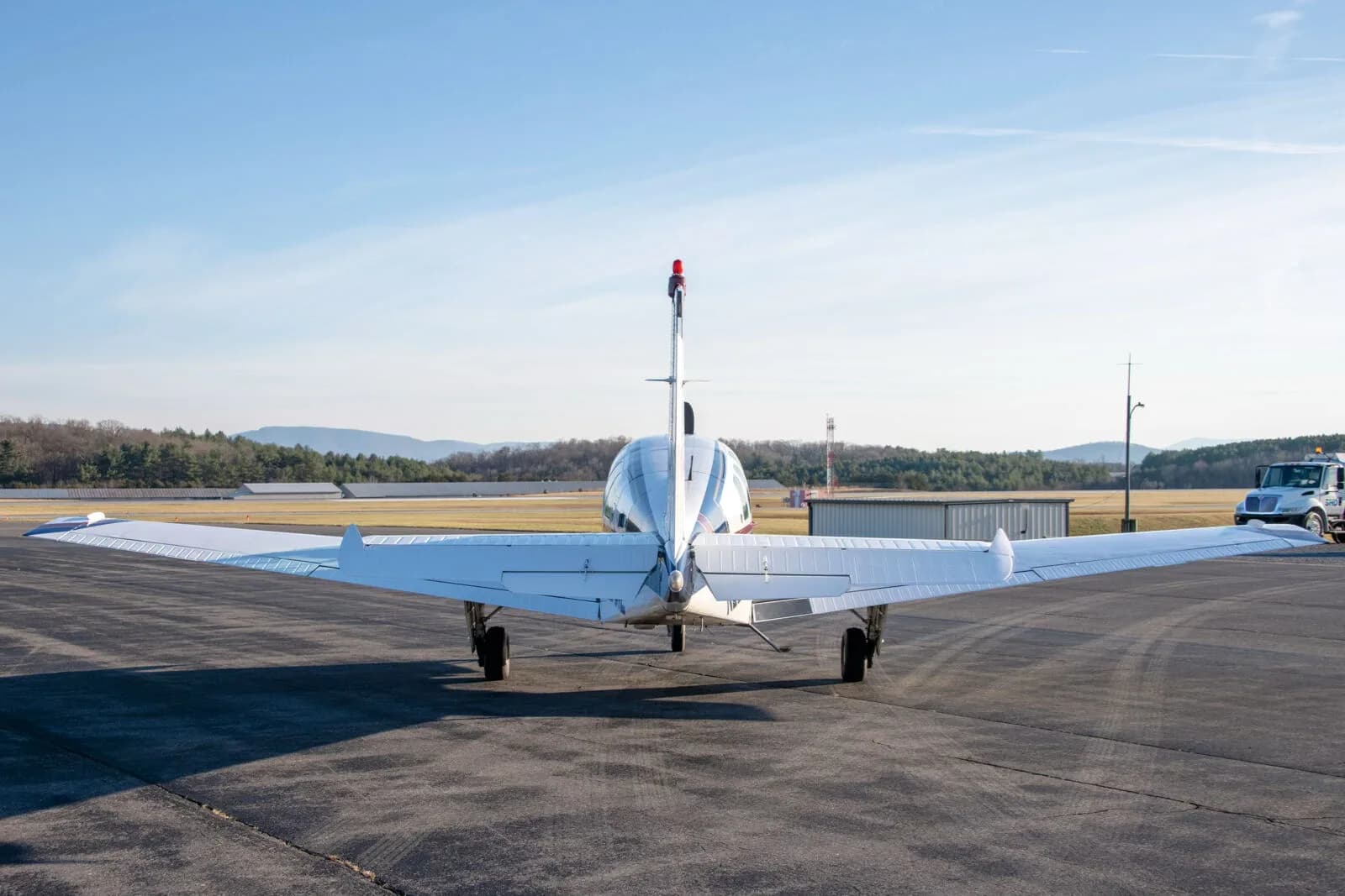 Rear view of a white Beechcraft Bonanza N2261L with blue and red stripes parked on an airfield.