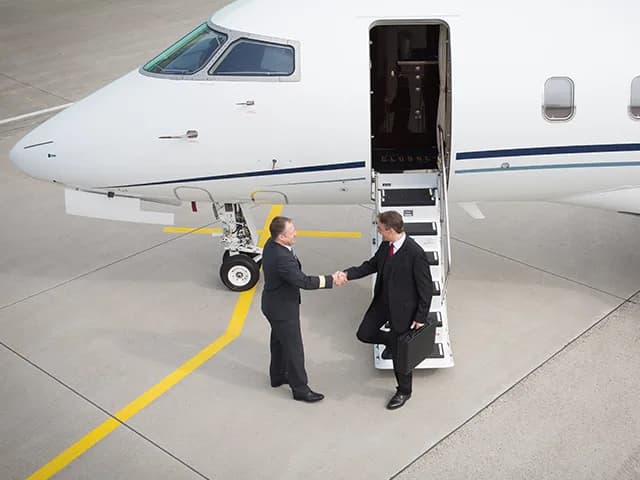 Two men shake hands at the base of the stairs of a private jet.