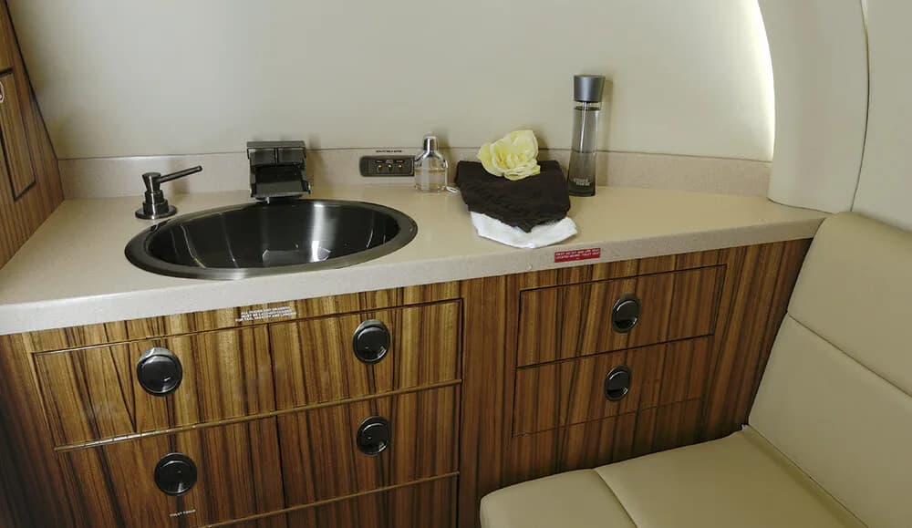 A view of the aircraft lavatory with a sink, faucet, and wooden cabinetry.