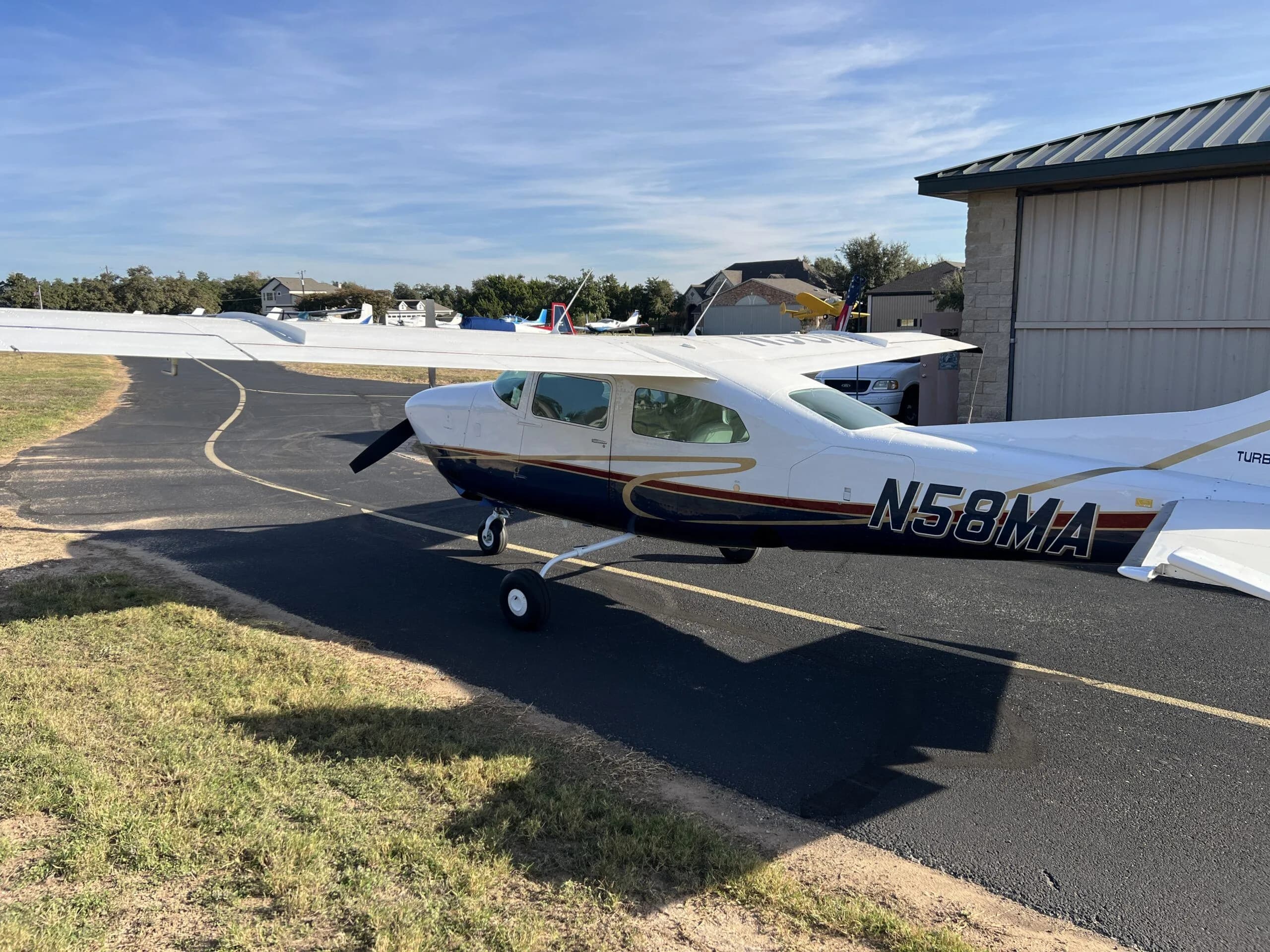 A side view of the white and blue Cessna 210, N58MA, parked on an asphalt taxiway.