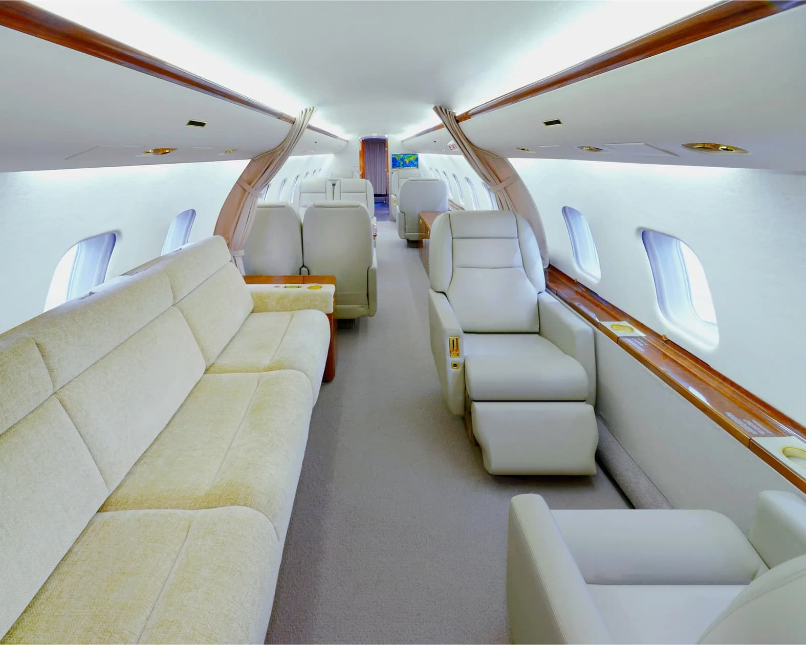A wide view of a private jet's cabin interior featuring a long beige sofa and individual reclining seats.