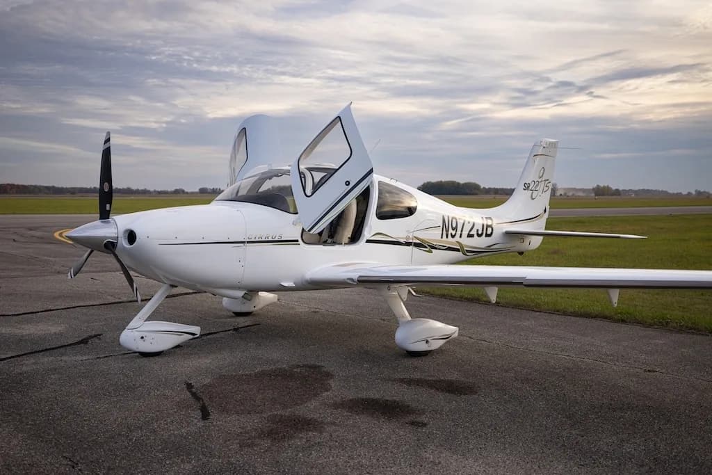 A white Cirrus SR22T aircraft with registration N972JB is parked on an airfield with its doors open.